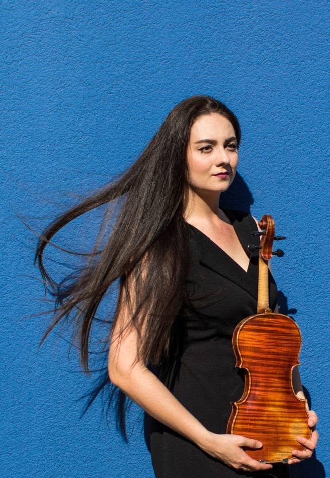 Musician portrait holding a violin against a blue wall