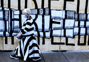 A woman walking dressed in bnw patterns that fit the wall behind her