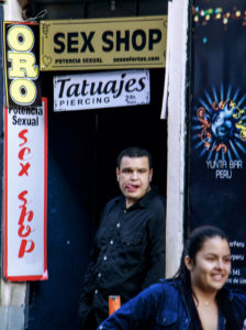 A man in the sex shop enterance pull his tounge when a girl goes by