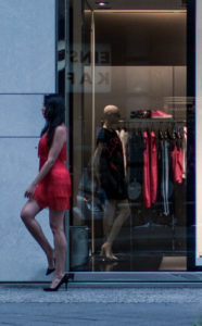 A model is crossing her legs in a similar pose to a window display mannequin behind