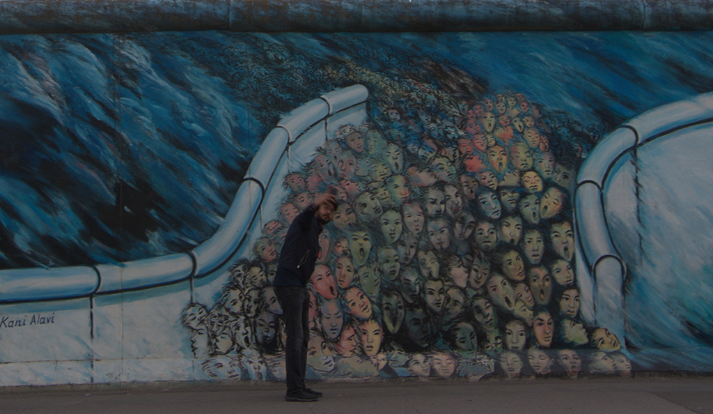 East side gallery street photo of a man making selfie next to the wall
