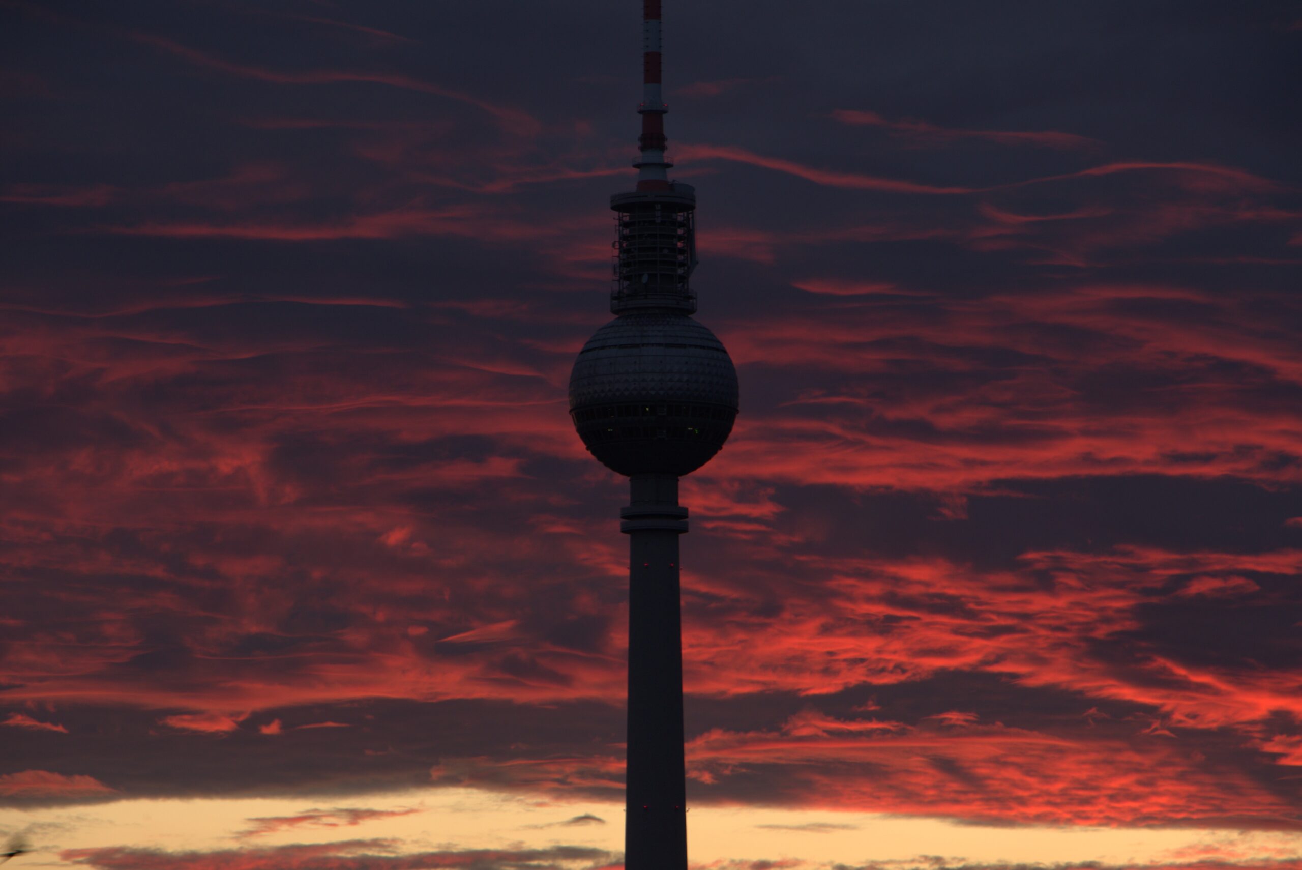Berlin's TV Tower silhouetted against red clouds and a pale band of sunset sky.
