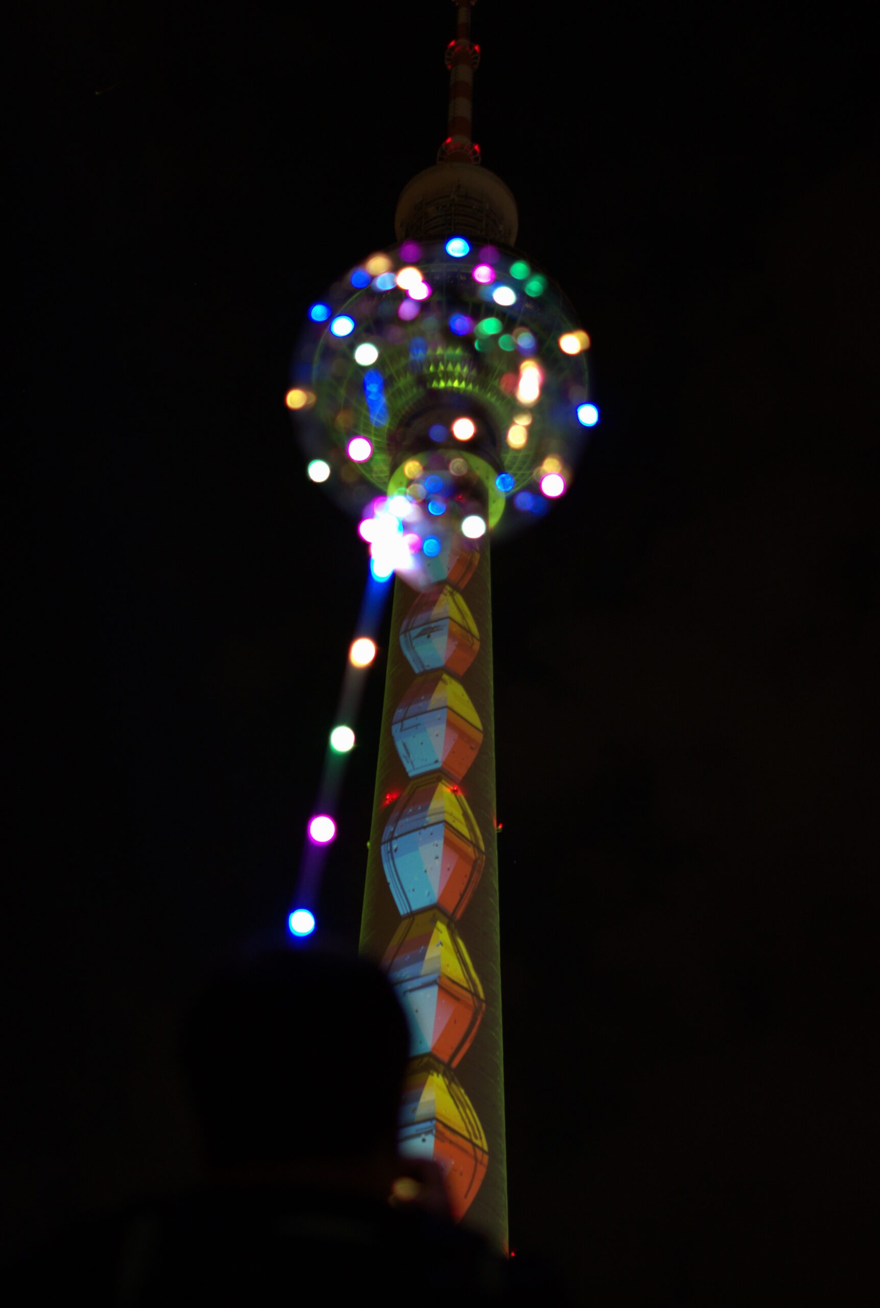 Multicoloured LED balloon lights overlap Berlin's illuminated TV Tower at night.